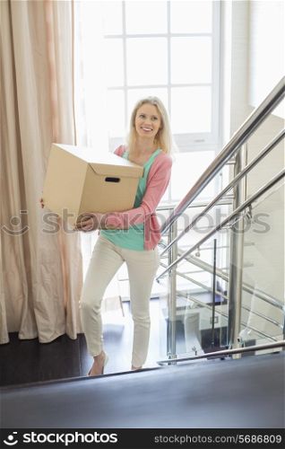 Smiling woman carrying cardboard box while moving up steps at new home