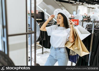 Smiling woman choosing hat in clothing store. Female person shopping in fashion boutique, shopaholic, shopper looking on garment. Smiling woman choosing hat in clothing store