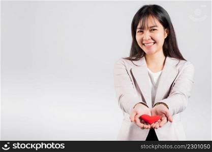 Smiling woman confidence showing holding red heart with her hand palm isolated white background, Asian happy portrait beautiful young female send love and happy valentine in studio shot, copy space