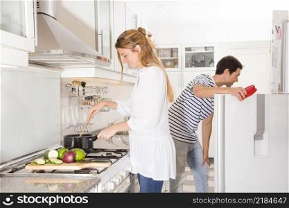smiling woman cooking vegetables while her husband opening refrigerator door
