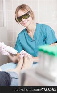 Smiling woman cosmetician in safety glasses working with laser during foot treatment