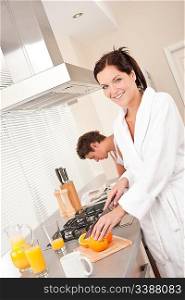 Smiling woman cutting oranges for breakfast in the kitchen