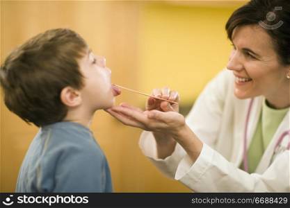 Smiling woman doctor examining child patient with tongue depressor