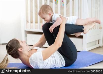 Smiling woman doing yoga exercise with her baby in living room