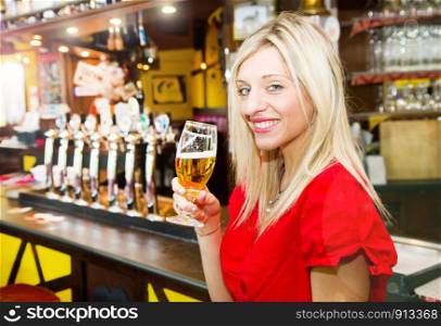 smiling woman drinking a fresh beer in a pub with friend