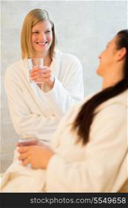 Smiling woman drinking water with friend at beauty spa