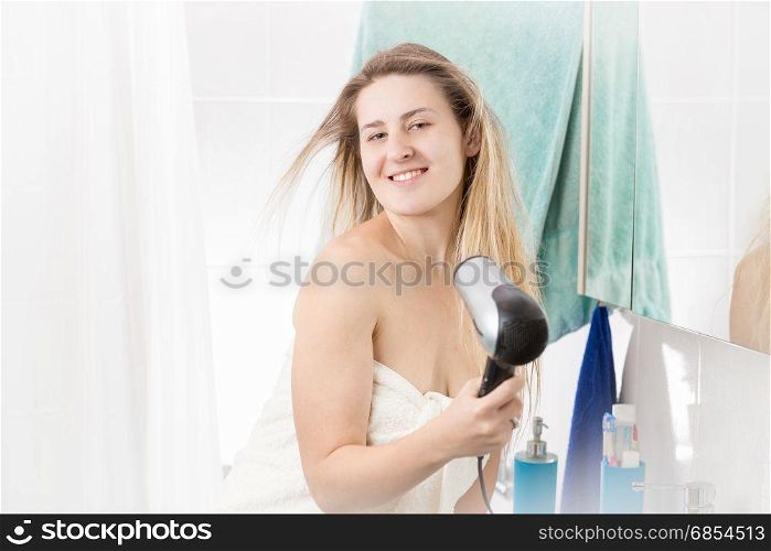 Smiling woman drying long blonde hair after having shower