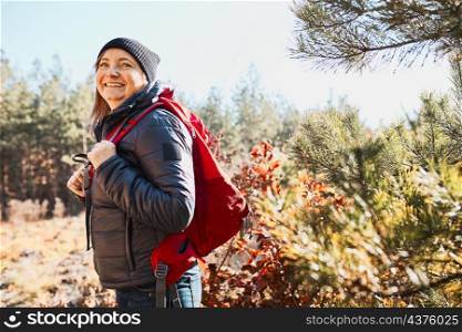 Smiling woman enjoying hike on sunny vacation day. Female with backpack walking through forest. Spending summer vacation close to nature