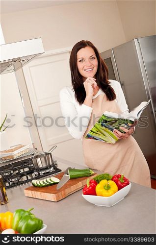 Smiling woman holding cookbook while cooking in the kitchen