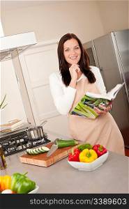 Smiling woman holding cookbook while cooking in the kitchen