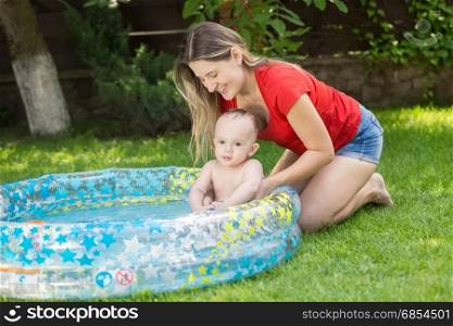 Smiling woman holding her baby boy in inflatable swimming pool at garden