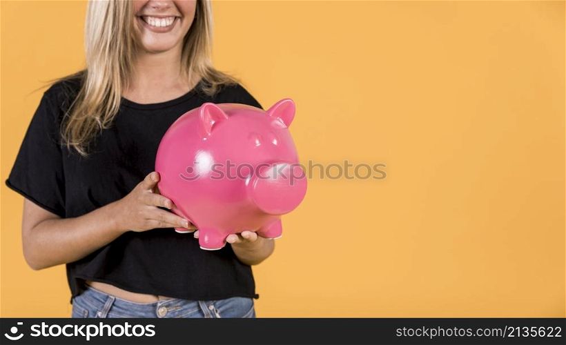 smiling woman holding pink piggy bank against bright backdrop