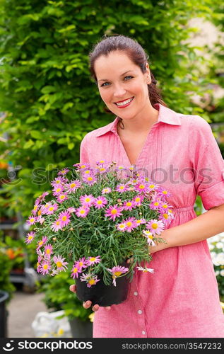 Smiling woman holding pink potted flower in garden center greenhouse