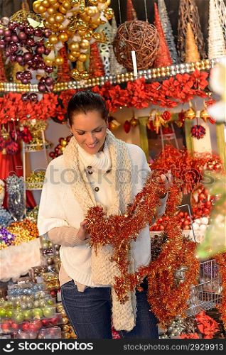Smiling woman holding shiny Christmas tinsel chain at shop