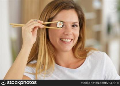 smiling woman holding sushi in front of eye with chopsticks