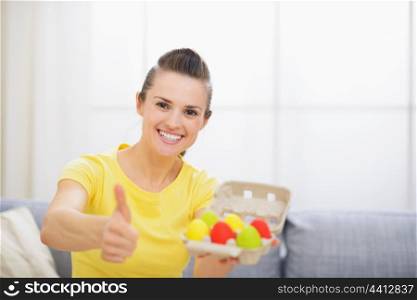 Smiling woman holding tray with colorful Easter eggs and showing thumbs up
