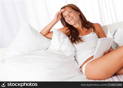 Smiling woman holding white book sitting on sofa
