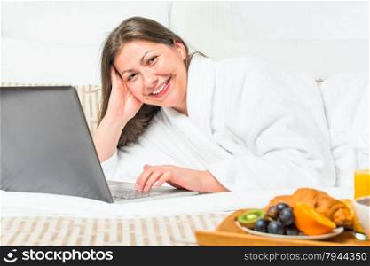 smiling woman in bed with a laptop and breakfast tray