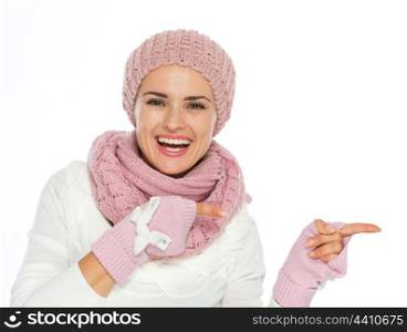 Smiling woman in knit scarf, hat and mittens pointing on copy space