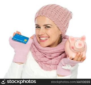 Smiling woman in knit winter clothing holding credit card and piggy bank