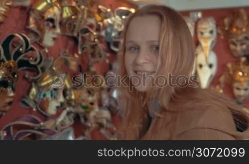 Smiling woman in store of Venetian masks trying on golden one. Preparation for carnival