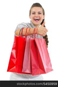 Smiling woman in sweater showing thumbs up with shopping bags