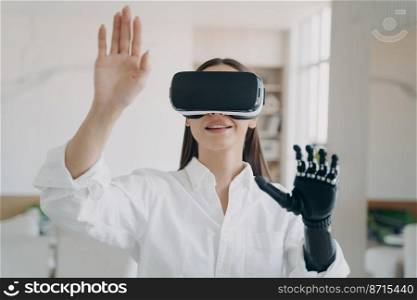 Smiling woman in VR glasses with disability interacting with augmented reality, touching virtual objects by bionic prosthetic arm. Girl testing new artificial limb. Medical high tech.. Girl in VR glasses interacts with augmented reality, touches virtual object by bionic prosthetic arm