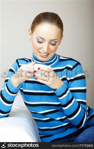 Smiling woman indoors in striped sweater holding cup with tea or coffee