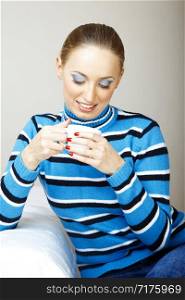 Smiling woman indoors in striped sweater holding cup with tea or coffee