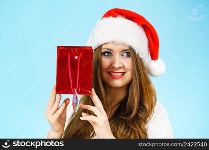 Smiling woman is happy to give Christmas gifts. Female wearing santa claus hat holding present red gift bag, on blue. Happy Christmas woman holds red gift bag