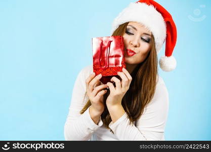 Smiling woman is happy to give Christmas gifts. Female wearing santa claus hat holding present red gift bag, on blue. Happy Christmas woman holds red gift bag