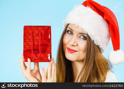 Smiling woman is happy to give Christmas gifts. Female wearing santa claus hat holding present red gift bag, on blue. Happy Christmas woman holds red gift bag