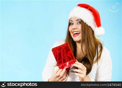 Smiling woman is happy to give Christmas gifts. Female wearing santa claus hat holding present red gift bag, on blue. Happy Christmas woman holds red gift bag