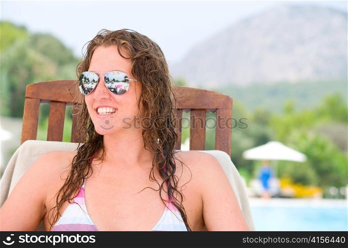 smiling woman is sitting on chair at poolside