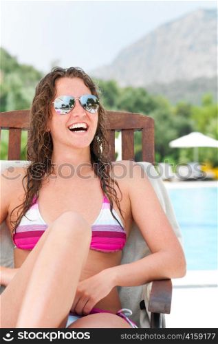 smiling woman is sitting on chair at poolside