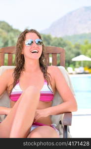 smiling woman is sitting on chair at poolside