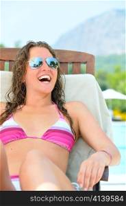 smiling woman is sitting on chair near a swimming pool