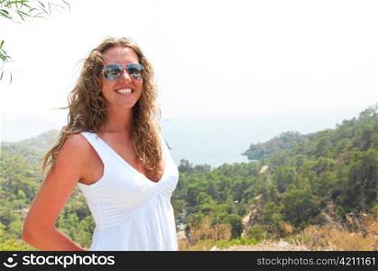 smiling woman is standing against green coastal mountains, snapshot style