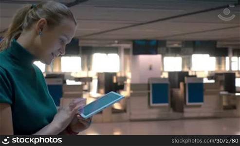 Smiling woman is writing something in tablet while standing by check-in gates in the airport.