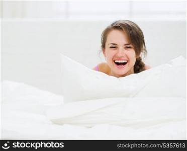 Smiling woman laying in bed and hiding behind pillow
