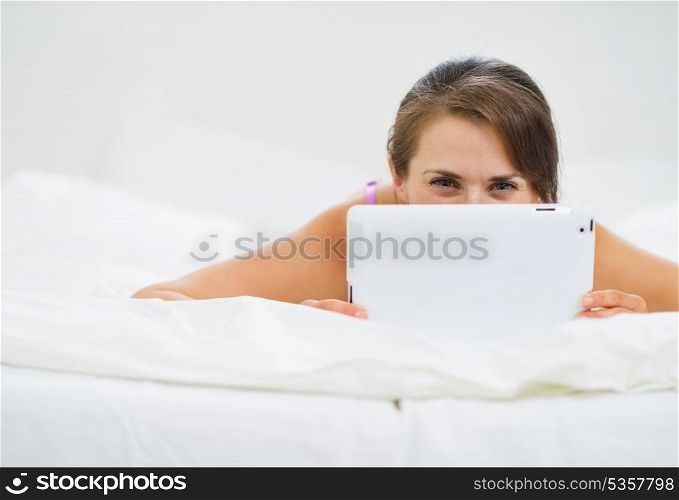 Smiling woman laying in bed and hiding tablet PC