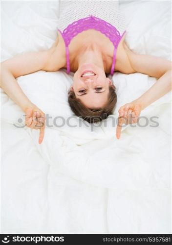 Smiling woman laying in bed and pointing on copy space
