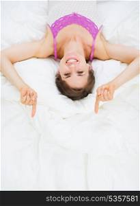 Smiling woman laying in bed and pointing on copy space
