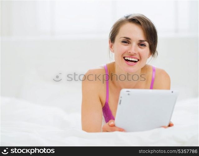 Smiling woman laying in bed and using tablet PC