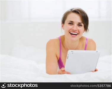 Smiling woman laying in bed and using tablet PC