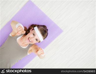 Smiling woman laying on fitness mat and pointing on you
