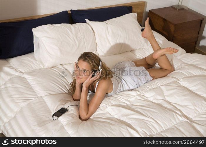 Smiling woman laying on modern bed in bedroom in morning listening to music on headphones