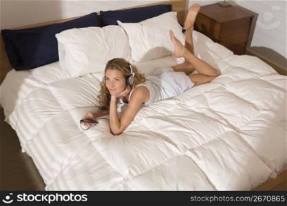 Smiling woman laying on modern bed in bedroom in morning listening to music on headphones