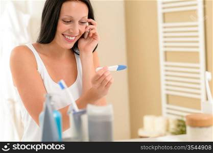 Smiling woman look positive pregnancy test calling phone in bathroom