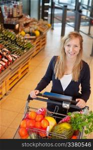 Smiling woman looking at camera while holding shopping cart in store